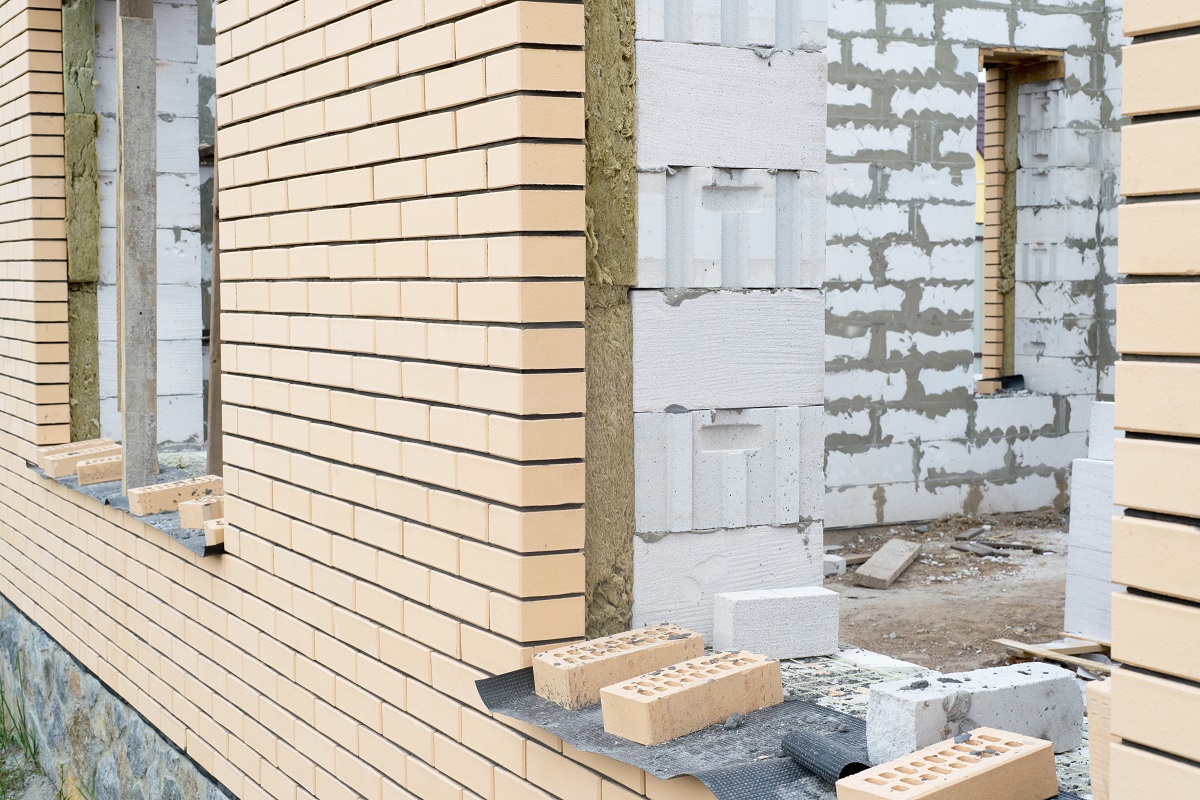 Кирпичная стена с уложенными кирпичами и строительными материалами на переднем плане.