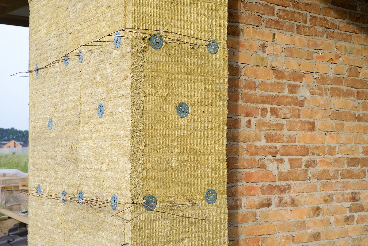 Кирпичная стена с минватой, прикрепленной к ней с помощью пластиковых дюбелей.