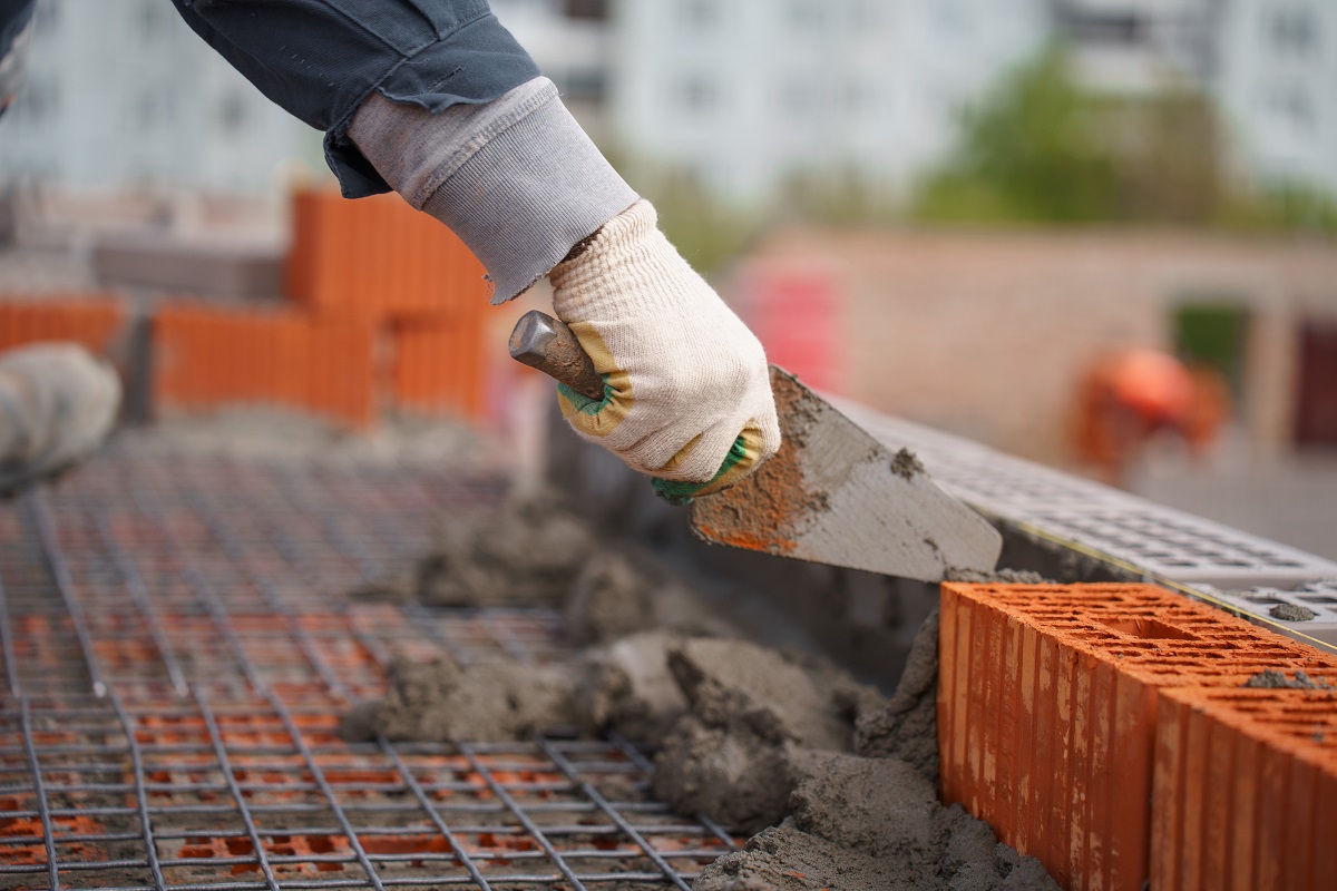 Строитель в перчатках наносит раствор на кирпичную кладку с помощью мастерка.