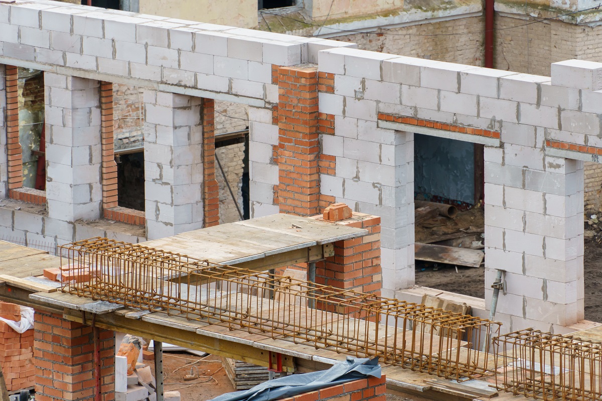 Строительство дома из газобетона. Видны стены из газобетонных блоков, деревянные балки и строительные материалы на полу.