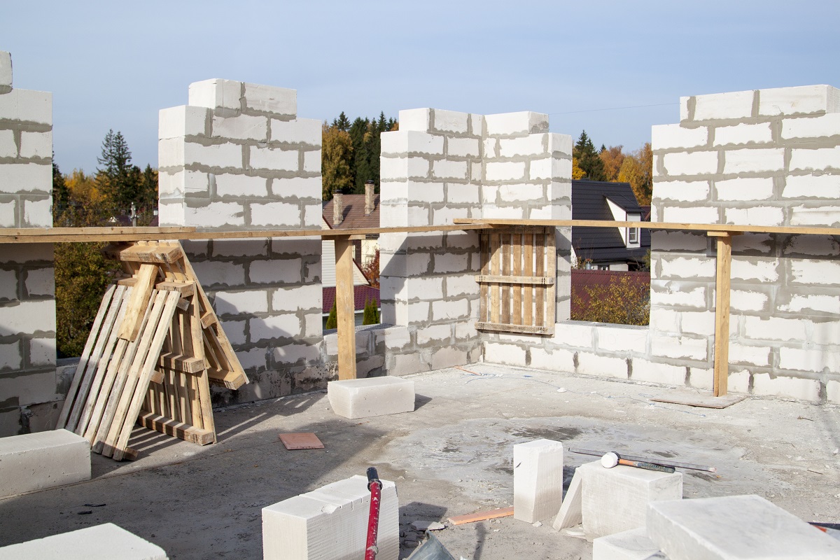 Строительство дома из газобетона. Видны стены из газобетонных блоков, деревянные балки и строительные материалы на полу.