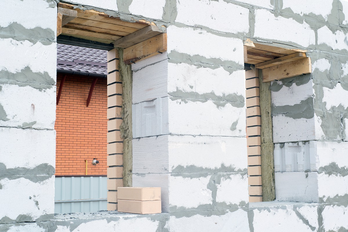 Процесс строительства дома из газобетона. Стены покрыты штукатуркой, видны деревянные балки для установки окон и дверей.